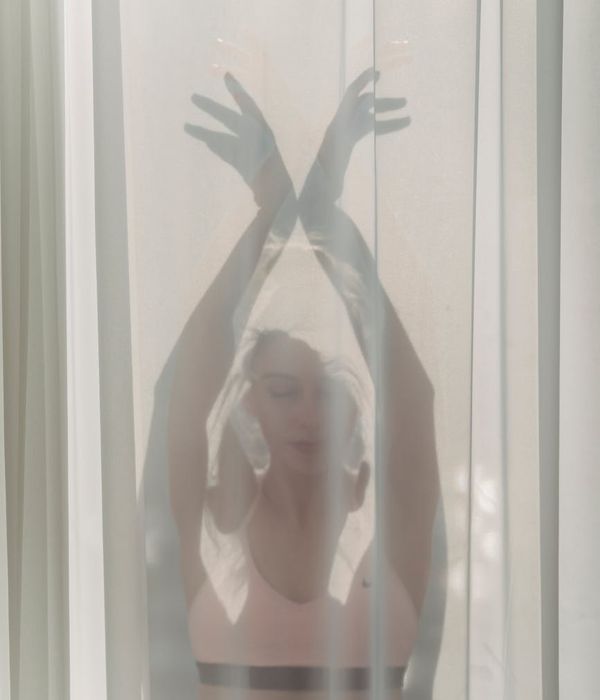 Woman in a calm yoga pose in a dark room with soft pink light.